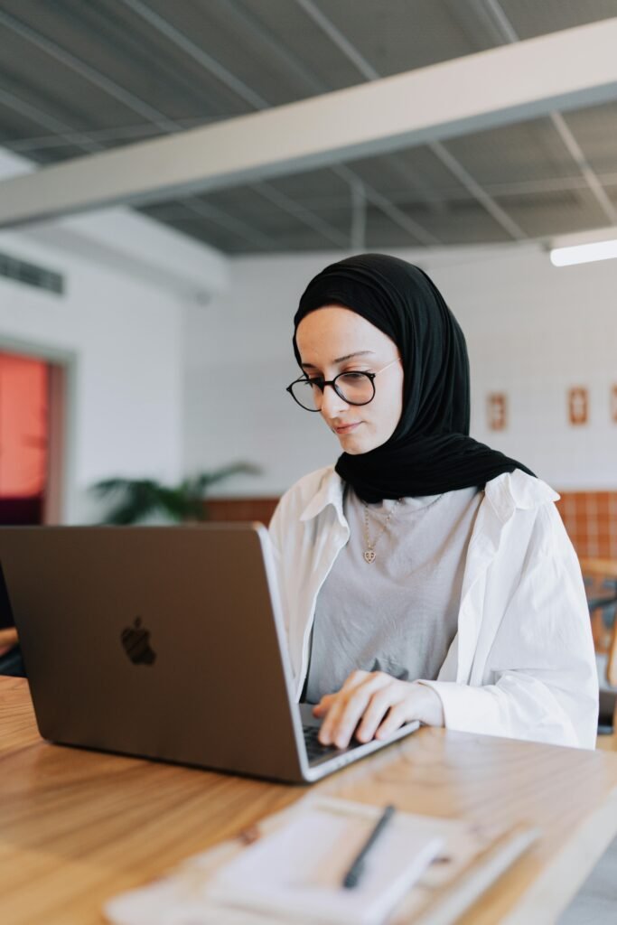 A young woman in a hijab using a laptop while sitting at a table, embodying a modern and professional setting.
